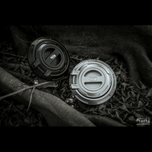 Load image into Gallery viewer, gas cap cover for jeep in black and silver color. 2 gas cap covers laying on the ground in leaves